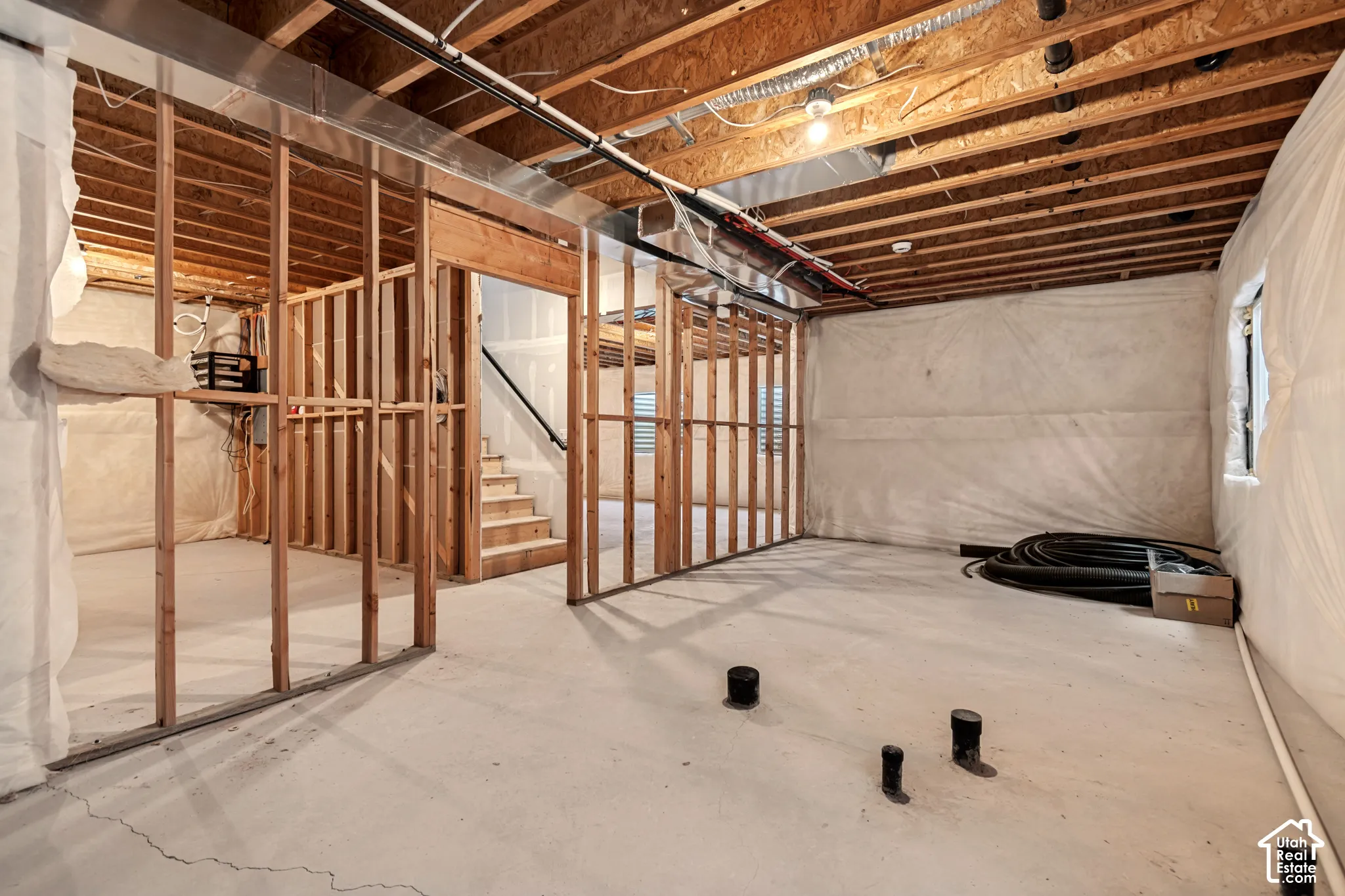 Unfinished basement featuring exposed wood framing, concrete flooring, and an open stairwell