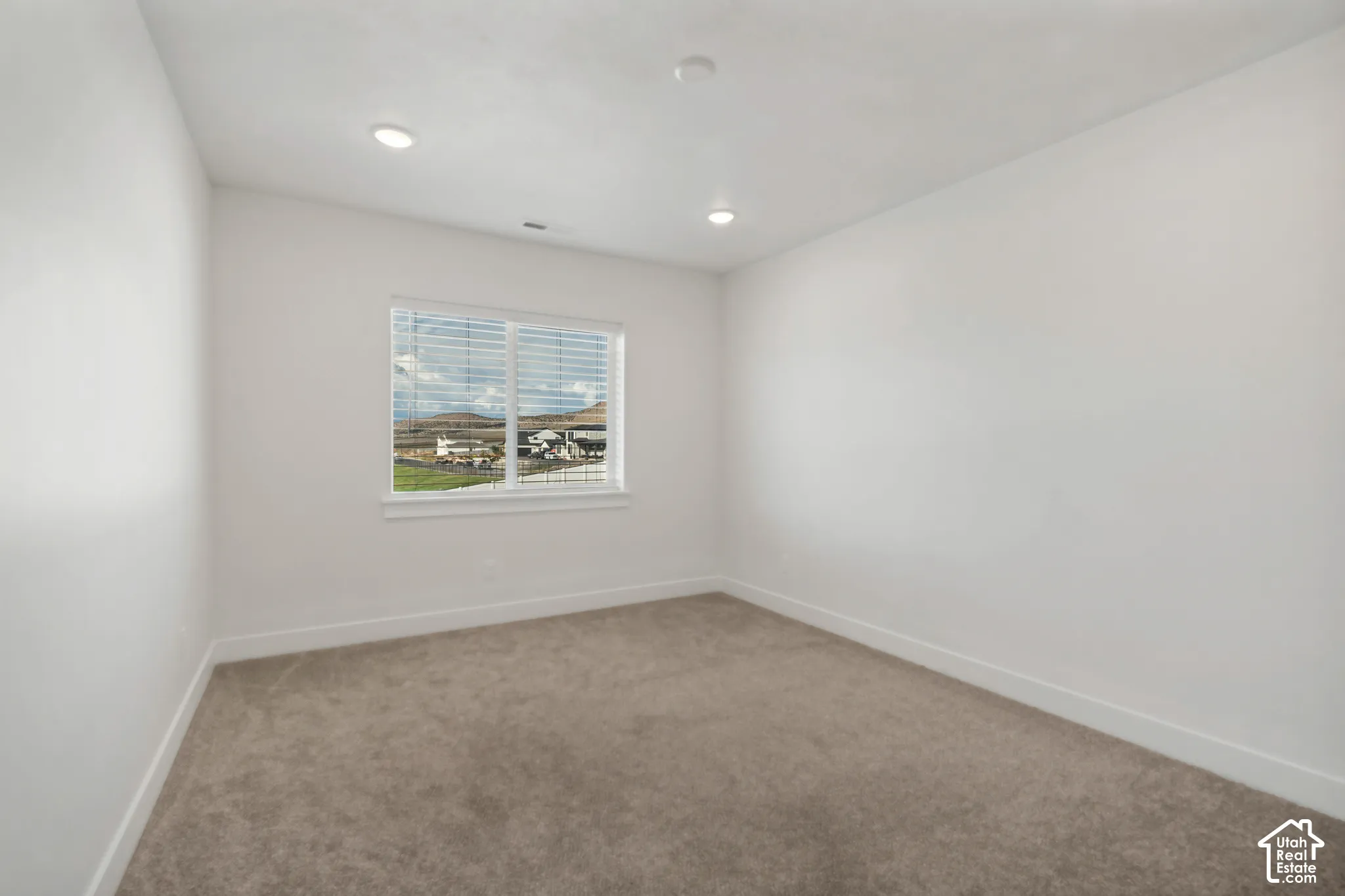 Recessed ceiling lighting, white walls, carpeted flooring, and a large window with blinds