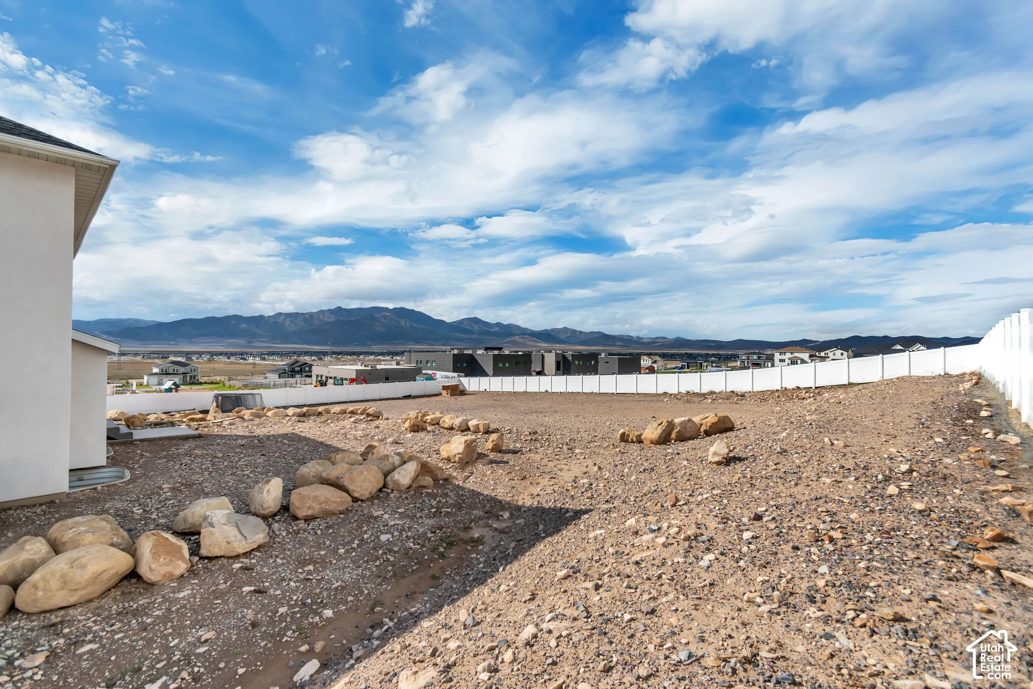 Expansive undeveloped lot featuring a white perimeter fence, natural rock accents, and distant mountain scenery