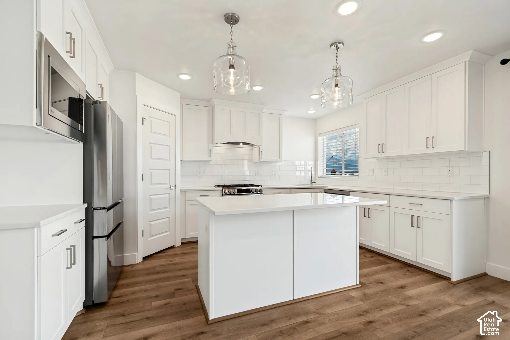 Contemporary kitchen featuring white cabinetry, stainless steel appliances, wood-finish flooring, white subway tile backsplash, and an island with a white countertop