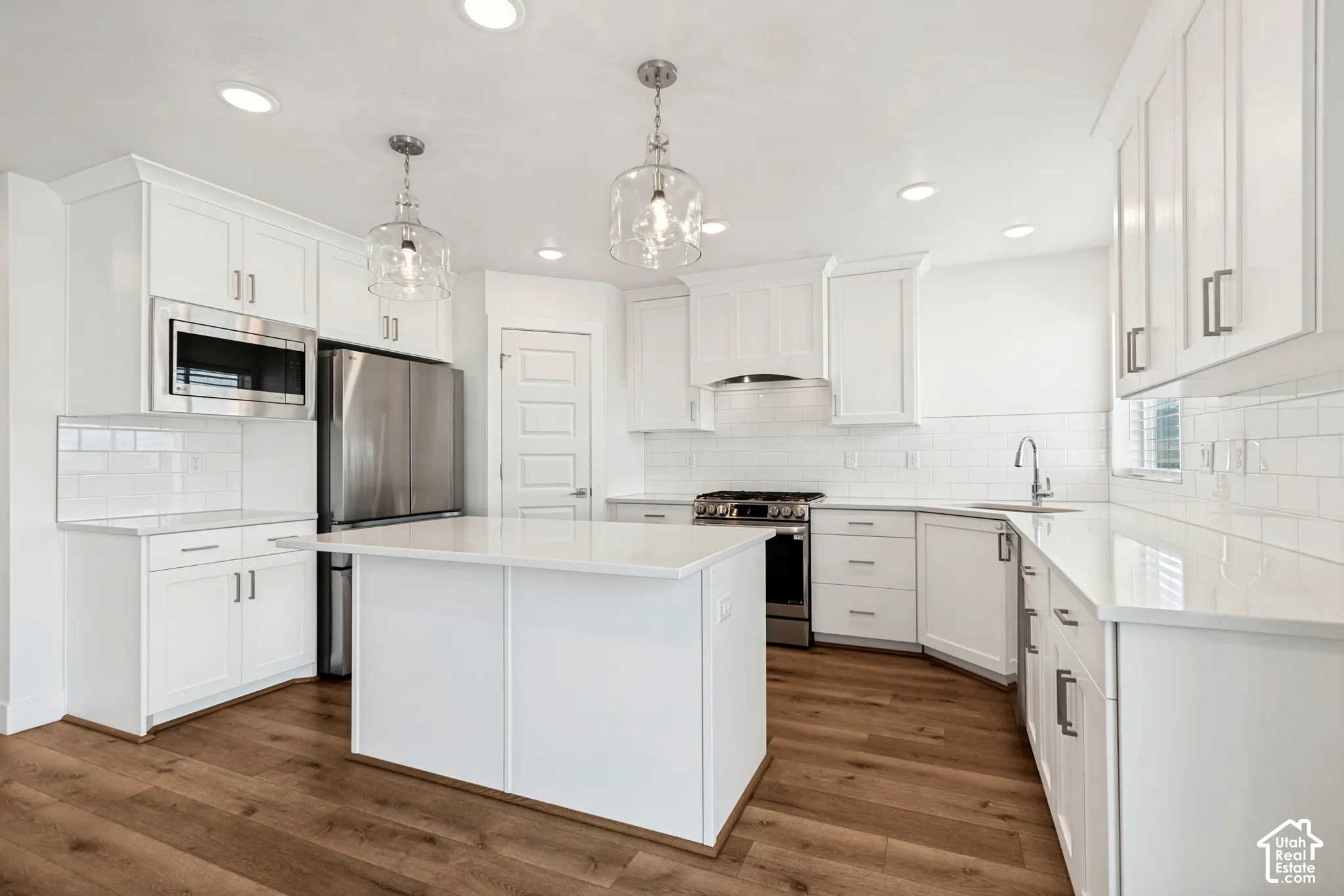 Kitchen featuring white shaker cabinetry, stainless steel appliances, a center island, wood-finish flooring, and pendant lighting