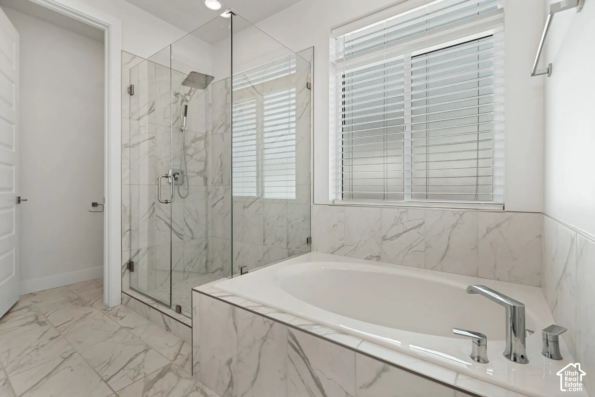 Glass-enclosed shower with a rainfall showerhead, white soaking tub, and tile surround, all featuring a white and gray veined pattern