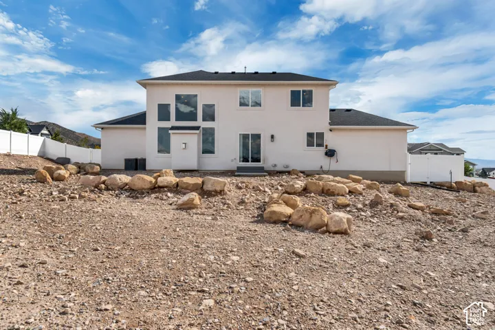 Rear elevation featuring a stucco exterior, dark roof, white vinyl fencing, and a combination of fixed and operable windows