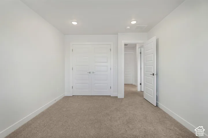 Recessed ceiling lighting, white walls, carpeted flooring, paneled interior doors, and a double-door closet