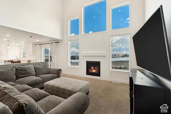 Vaulted ceiling with multiple windows, shiplap-style fireplace surround with mantel, built-in fireplace, light-toned carpeting, and sliding glass door