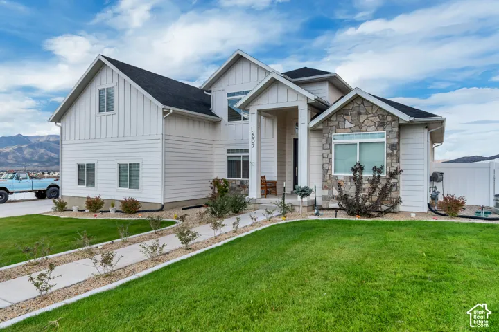 White siding exterior with stone accents, dark shingles, an arched entry, and a well-maintained lawn