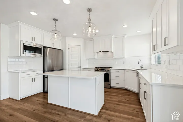Kitchen featuring white shaker cabinetry, stainless steel appliances, a center island, wood-finish flooring, and pendant lighting