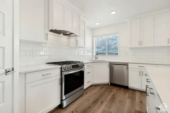 White shaker cabinetry, stainless steel appliances, subway tile backsplash, light-toned countertops, and wood-finish flooring