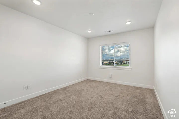 Recessed lighting, neutral-toned carpet, white walls, single window with blinds, and a distant cityscape