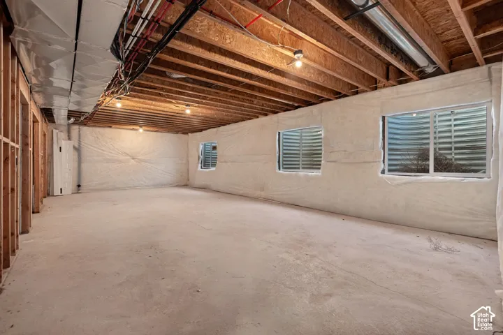 Unfinished basement with exposed wood joists, concrete flooring, and multiple egress windows