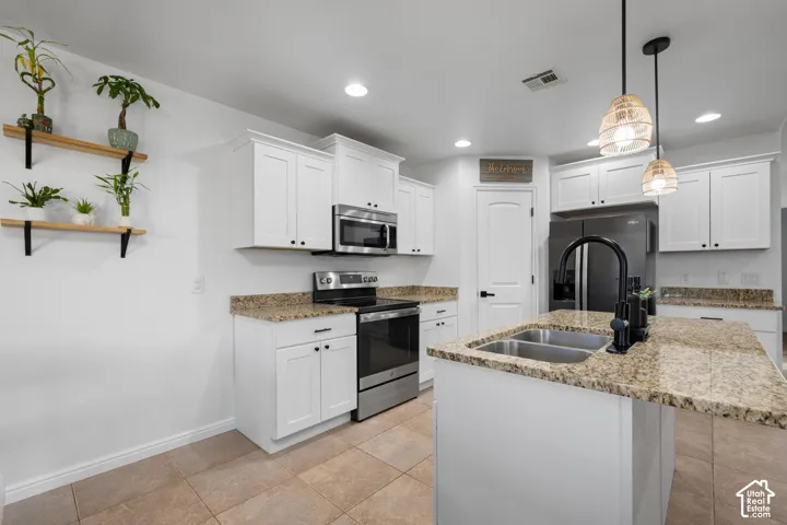White cabinetry with matte black hardware, stainless steel appliances, granite countertops, and a kitchen island with a double basin sink
