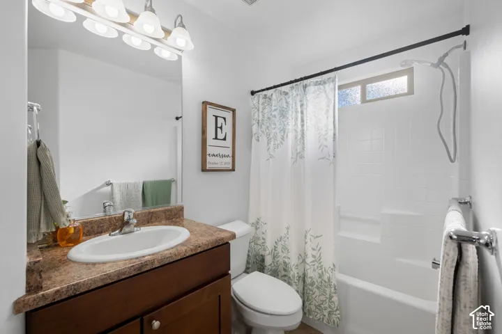 Vanity with a laminate countertop and undermount sink, overhead lighting fixture, tiled tub/shower combination, and a high window