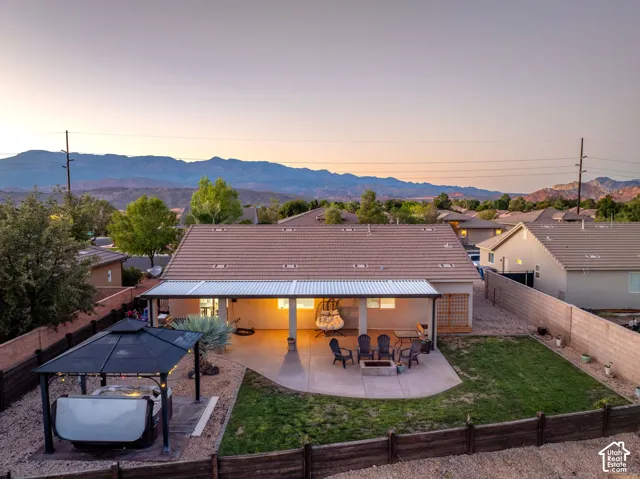 Expansive backyard featuring a covered patio, concrete hardscaping, fire pit, and lawn area