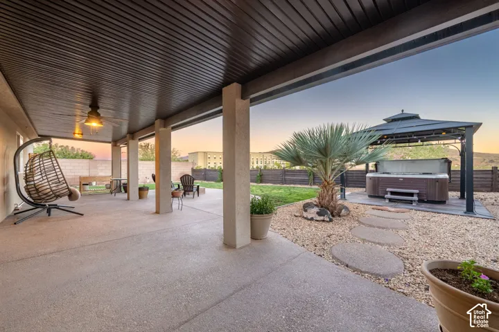 Expansive covered patio with concrete flooring, supported by robust pillars, featuring a built-in ceiling fan