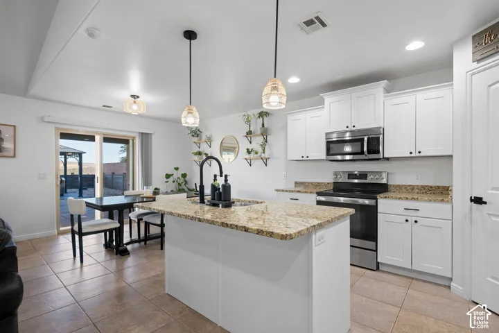 Kitchen featuring a central island with a sink, white cabinetry, granite countertops, and stainless steel appliances