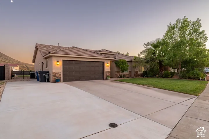 Stucco exterior with stone accents, attached garage, concrete driveway, front lawn, and mature landscaping