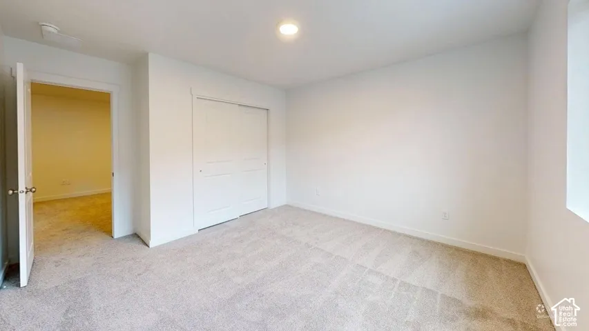 Light-toned wall-to-wall carpeting, white painted walls, recessed ceiling lighting, and a bi-fold closet door