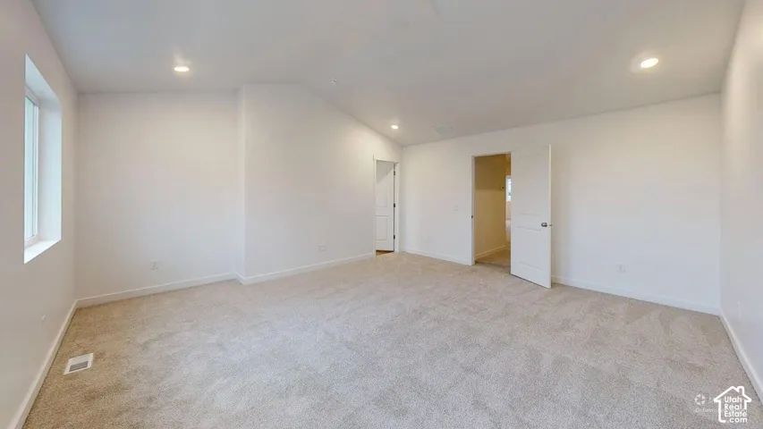 Expansive carpeted room featuring white walls, recessed ceiling lighting, and a white framed window