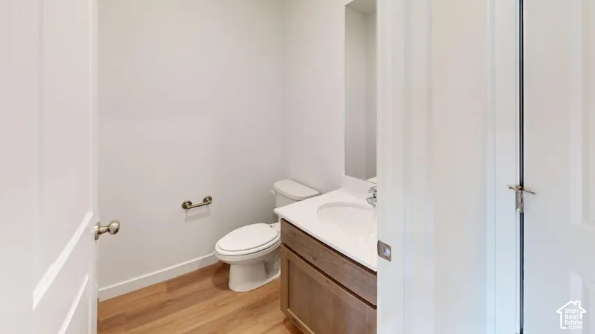 Wood-finish flooring, white walls, and a vanity with an integrated sink and mirror