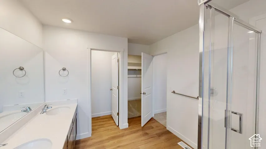 Dual vanity with integrated sinks, wood-finish flooring, recessed lighting, glass-enclosed shower, and built-in closet shelving