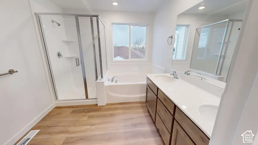 Wood-finish flooring, dual basin vanity with quartz-style countertop, built-in soaking tub, and enclosed shower with glass door