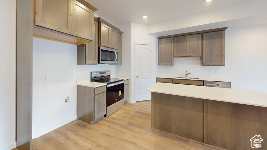 Kitchen featuring wood-finish flooring, light-toned cabinetry, a central island with a light countertop, stainless steel appliances, and a white subway tile backsplash