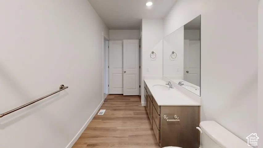 Dual sink vanity with a light countertop, wood-finish flooring, and recessed lighting