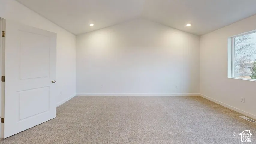 Vaulted ceiling with recessed lighting, light-toned carpet flooring, white walls, and a large window