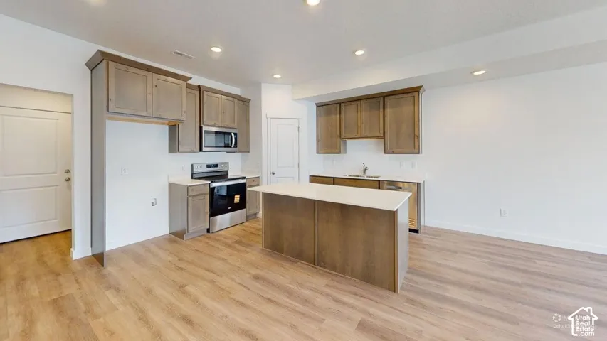 Kitchen featuring wood-finish flooring, recessed lighting, a center island with a white countertop, stainless steel appliances, and wood cabinetry