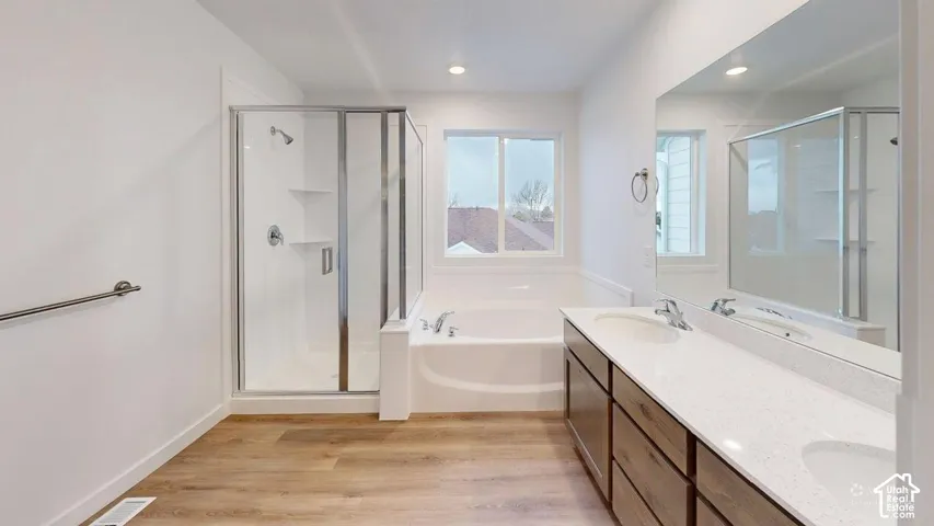 Wood-finish flooring with a built-in shower, soaking tub, dual sink vanity, and integrated lighting
