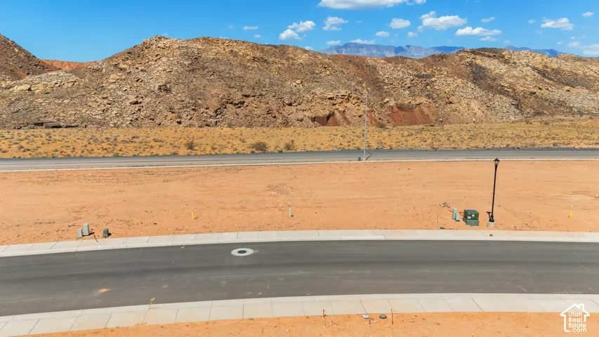 Paved street with concrete sidewalk, street lamp, utility box, and expansive desert scenery