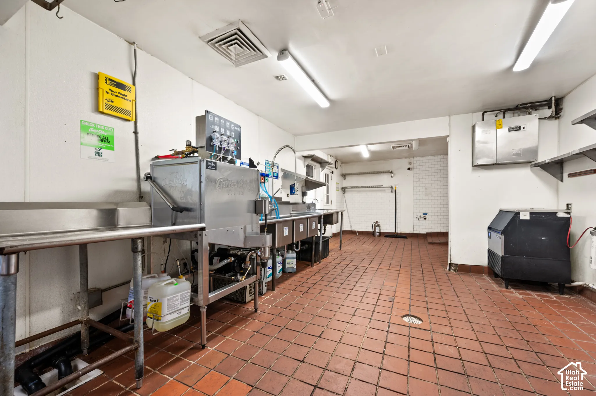 Commercial kitchen space featuring a tiled floor, stainless steel countertops, multiple sinks, and a dishwashing station