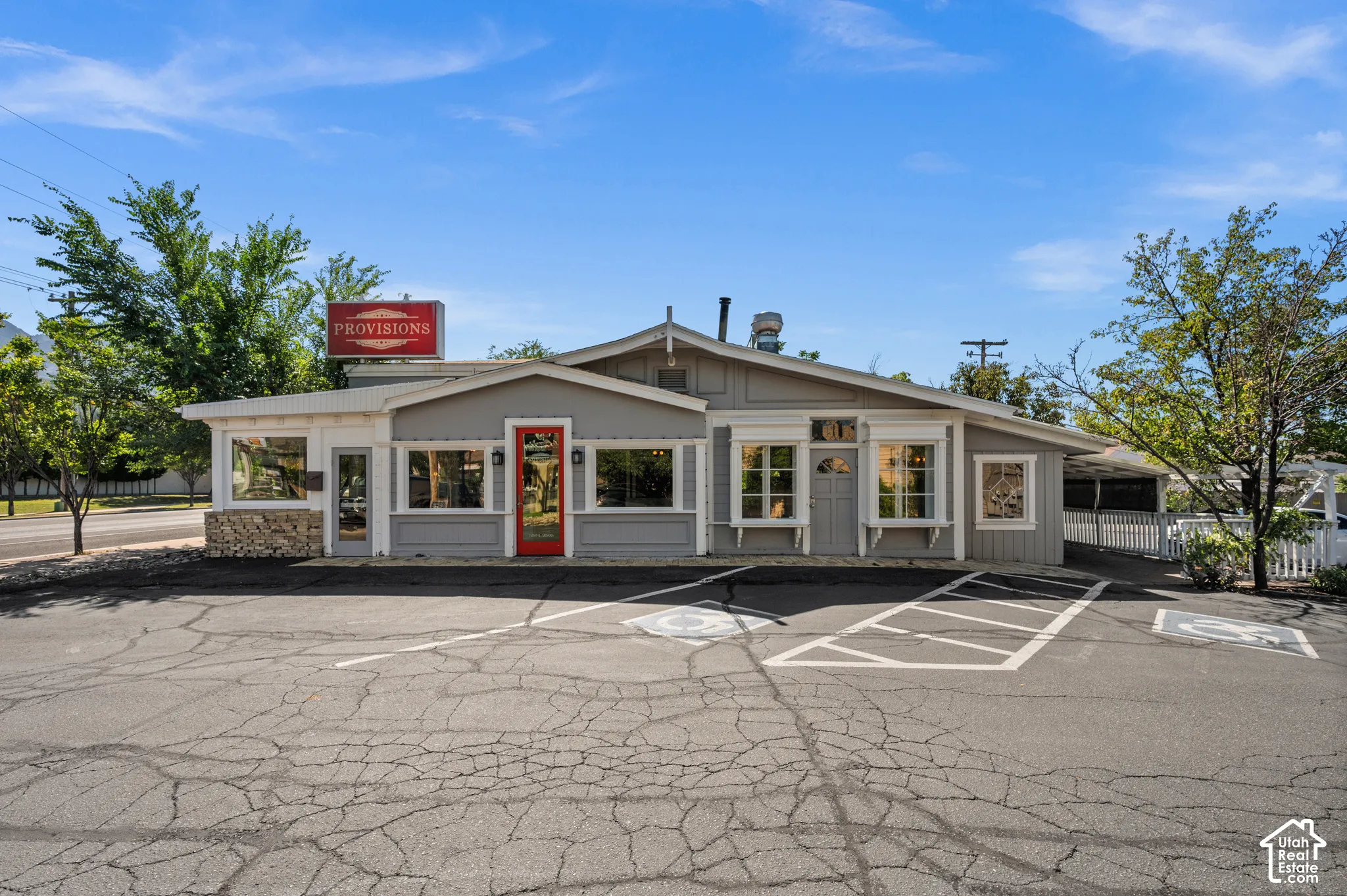 Gray exterior with stone veneer accents, multiple large windows, a red front entry door, and an on-site parking area