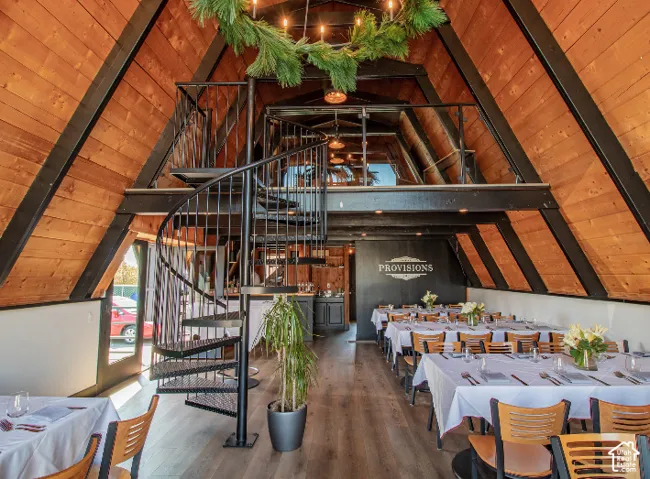 Vaulted ceiling with wood paneling, exposed structural beams, spiral staircase with metal railing, upper-level mezzanine, and wood-finish flooring