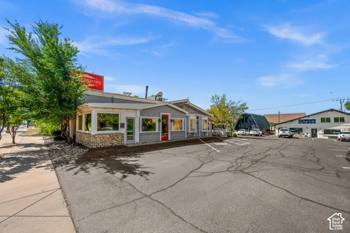 Asphalt parking lot, single-story commercial building, stone-clad facade, red entry door, multiple commercial windows