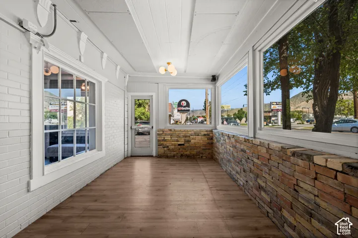 Sunroom with wood-finish flooring, white painted brick walls, and stacked stone accents