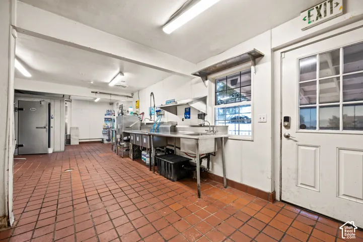 Commercial kitchen space featuring stainless steel work surfaces, a multi-compartment sink, and a walk-in cold storage unit