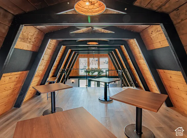 Vaulted wood-paneled ceilings with exposed black beams, wood-finish flooring, and a glass-paneled railing system