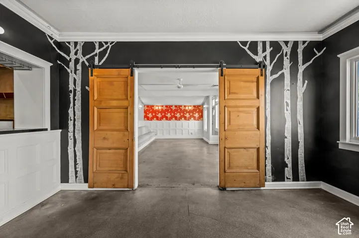 Concrete flooring, decorative wall mural, crown molding, wood paneling, paneled barn doors