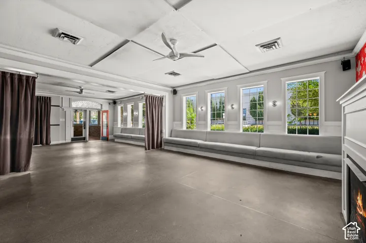 Spacious room featuring polished concrete flooring, built-in bench seating along a windowed wall, and a fireplace with a white mantel