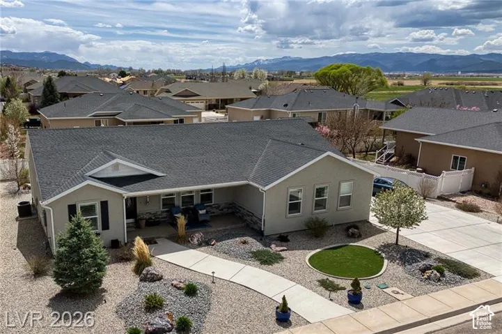 Stucco exterior featuring a dark asphalt shingle roof, concrete driveway, concrete pathway, and landscaped front yard with decorative rock and plantings