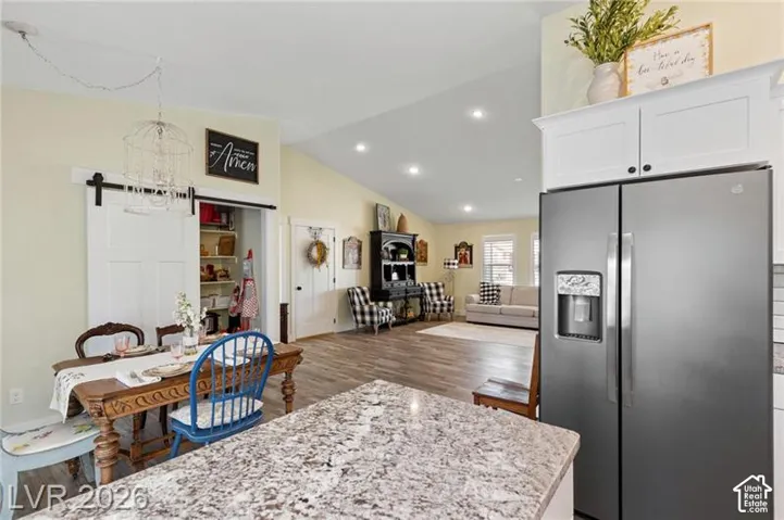 Vaulted ceiling, recessed lighting, wood-finish flooring, white flat-panel cabinetry, and a sliding barn door