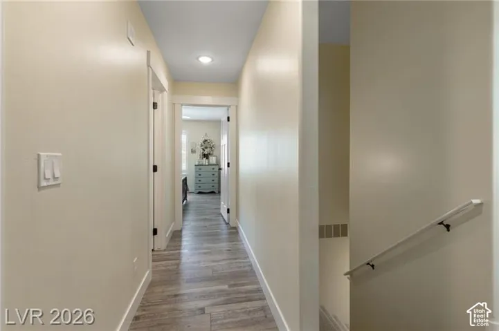 Hallway featuring wood-finish flooring, recessed lighting, and a white handrail