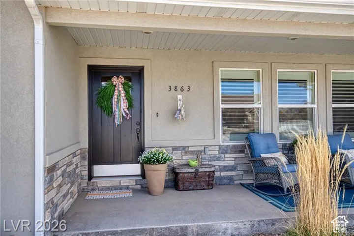 Covered front porch featuring a dark entry door, stone veneer detailing, multiple windows, and exterior stucco finish