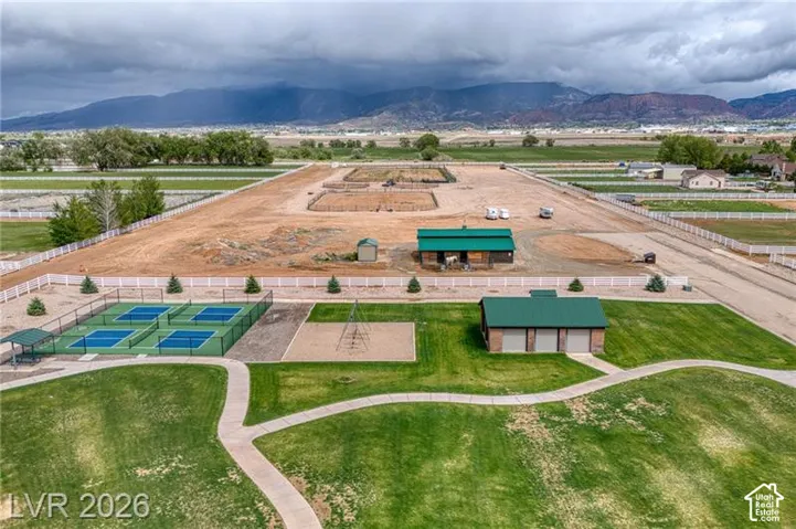 Four pickleball courts with perimeter fencing, a covered seating area, a large manicured lawn, and a playground area