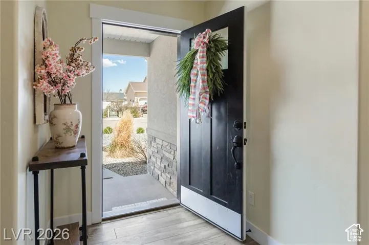 Wood-finish flooring, solid panel entry door, stone accent exterior, and a covered entry