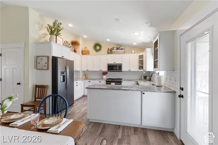Kitchen featuring wood-finish flooring, white cabinetry, recessed lighting, subway tile backsplash, and a large central island with a solid surface countertop