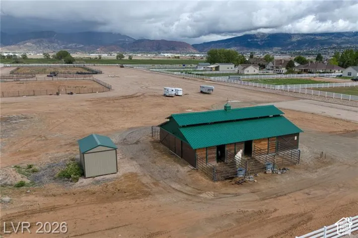 Barn structure with a green metal roof, multiple fenced enclosures, and an additional storage shed