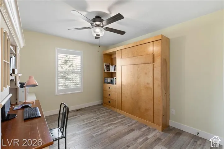 Built-in cabinetry with integrated shelving, ceiling fan with light fixture, window with plantation shutters, wood-finish flooring