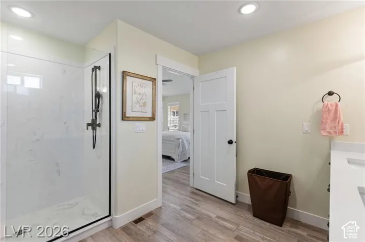 Glass-enclosed shower with white marble-patterned walls, wood-finish flooring, recessed lighting, and a solid panel interior door